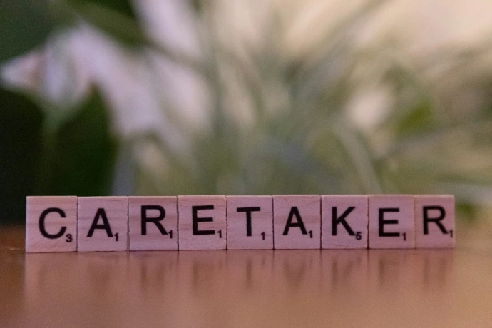 A wooden block spelling carettaker on a table